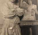 Photograph of Ilicio Joni, posing with his arms folded in front of a painting on an easel
