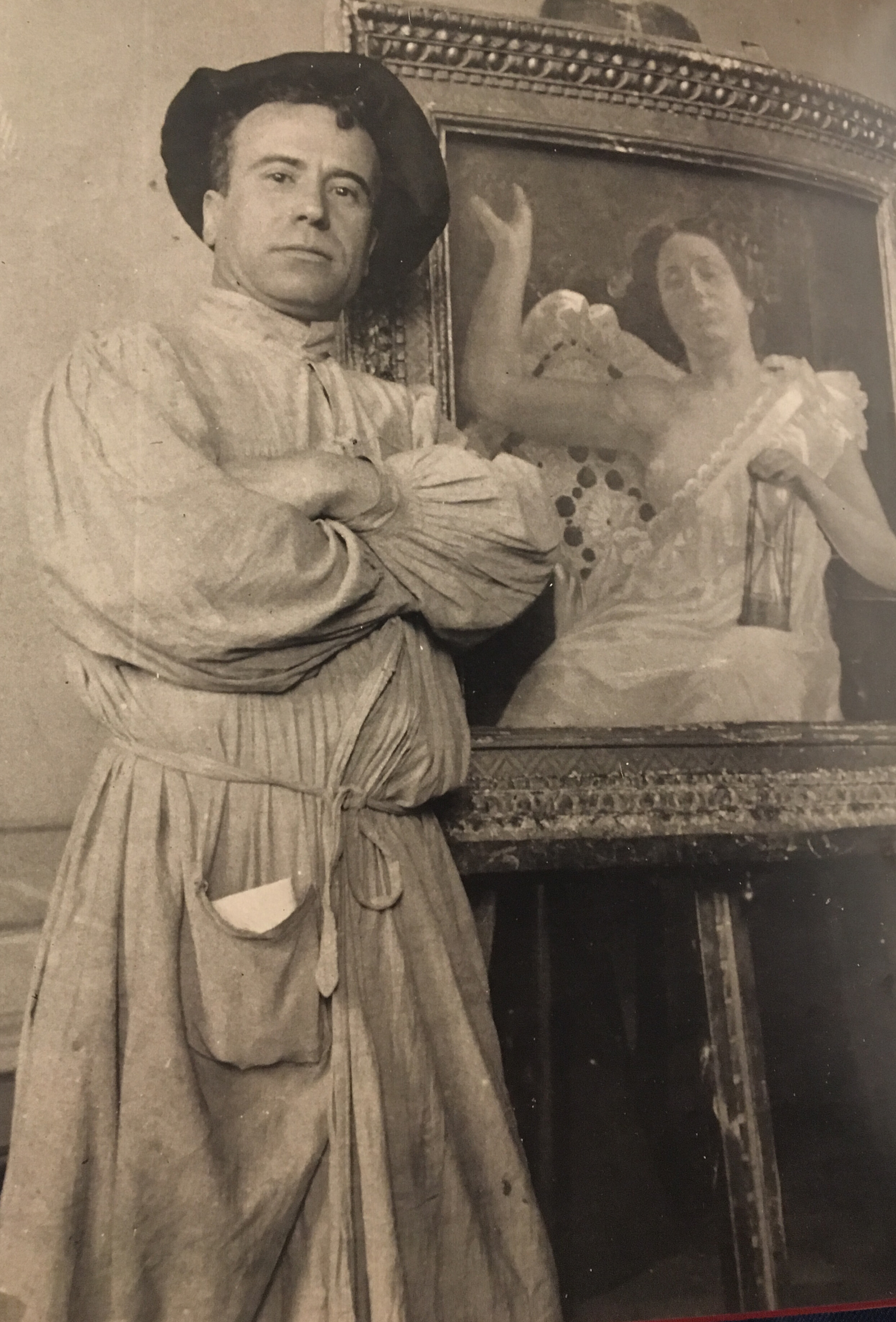 Photograph of Ilicio Joni, posing with his arms folded in front of a painting on an easel