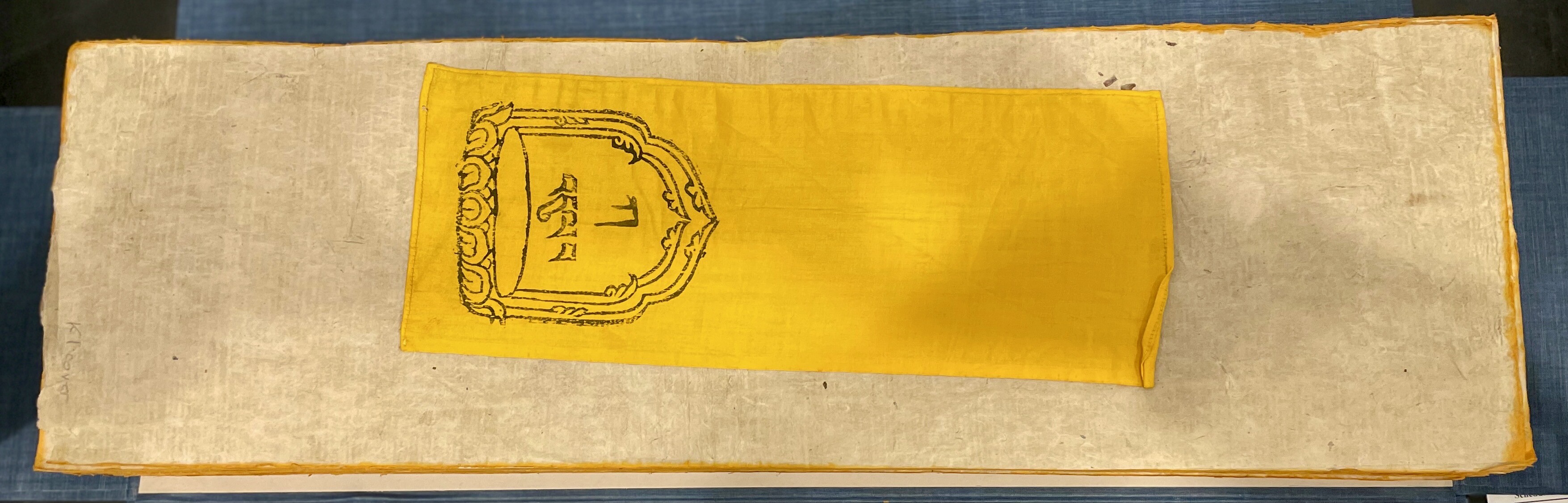 The cover of the Tibetan Kanjur with black text in a cartouche printed on yellow fabric..