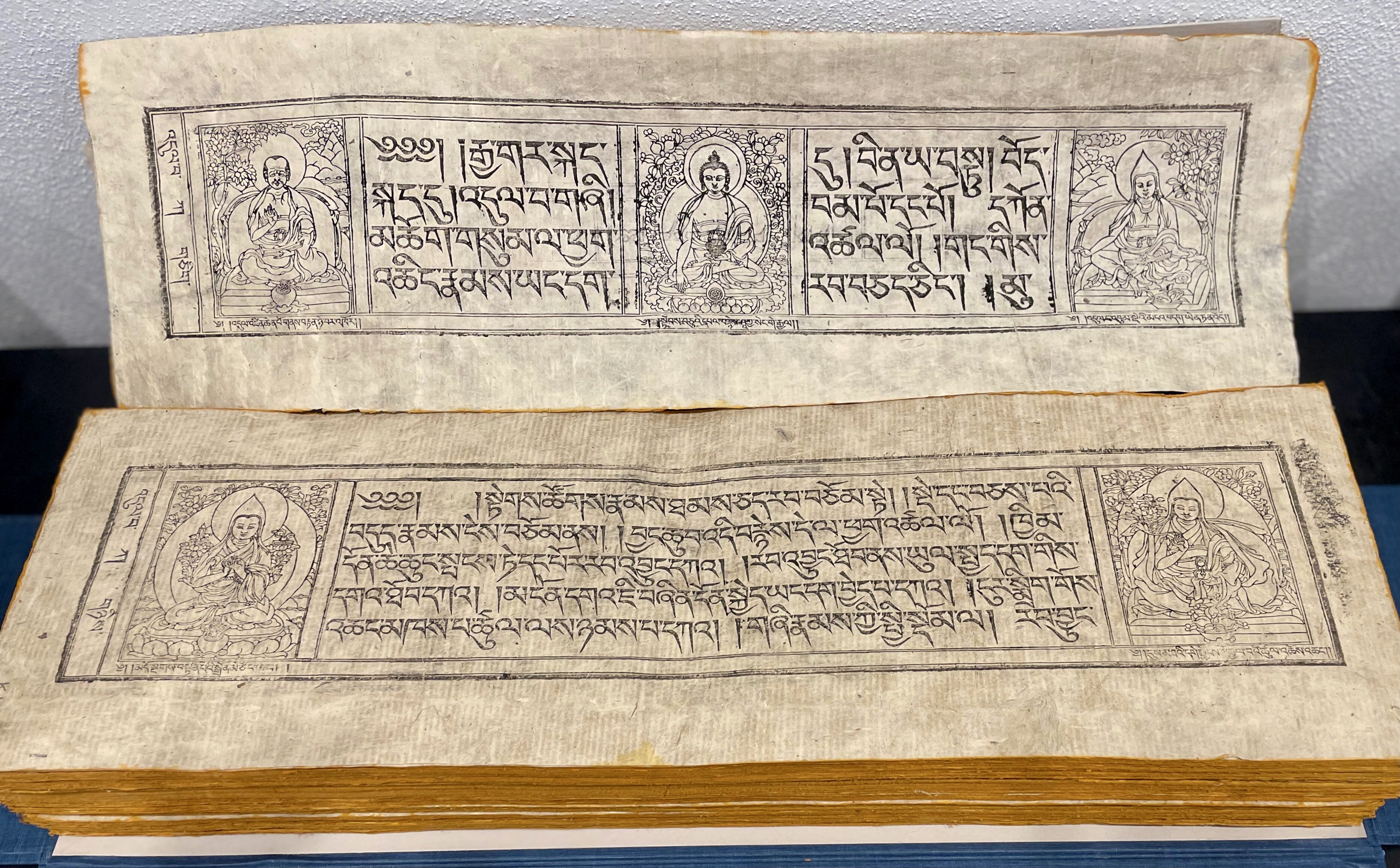 An image of two leaves of the Kanjur printed with text in Tibetan and five woodcuts of various holy figures.
