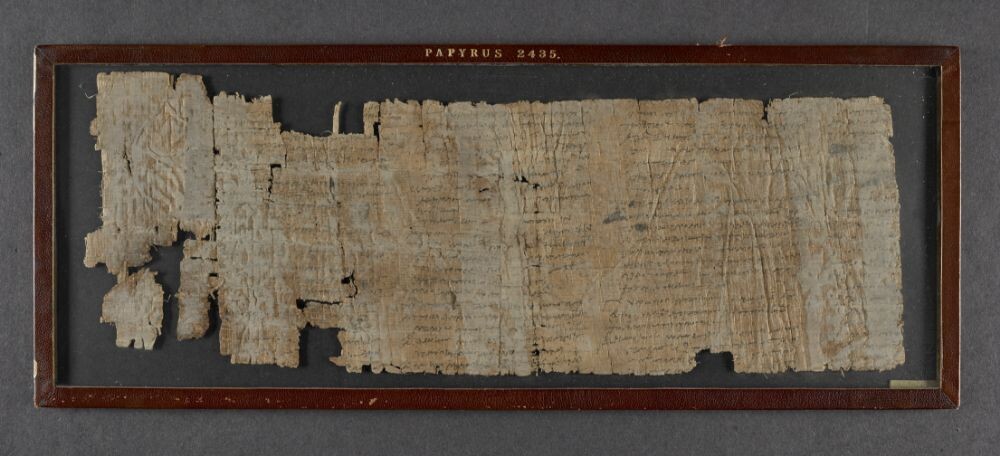 An unrolled papyrus fragment. Papyrus is tan with faint black letters in Greek.